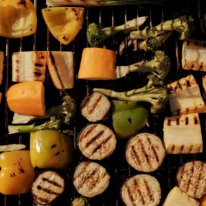 Assorted grilled vegetables including peppers, eggplant, and broccoli on a barbecue grill.