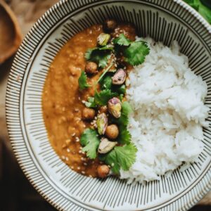 Delicious vegan rice bowl featuring lentil curry, topped with pistachios, cilantro, and sesame seeds.