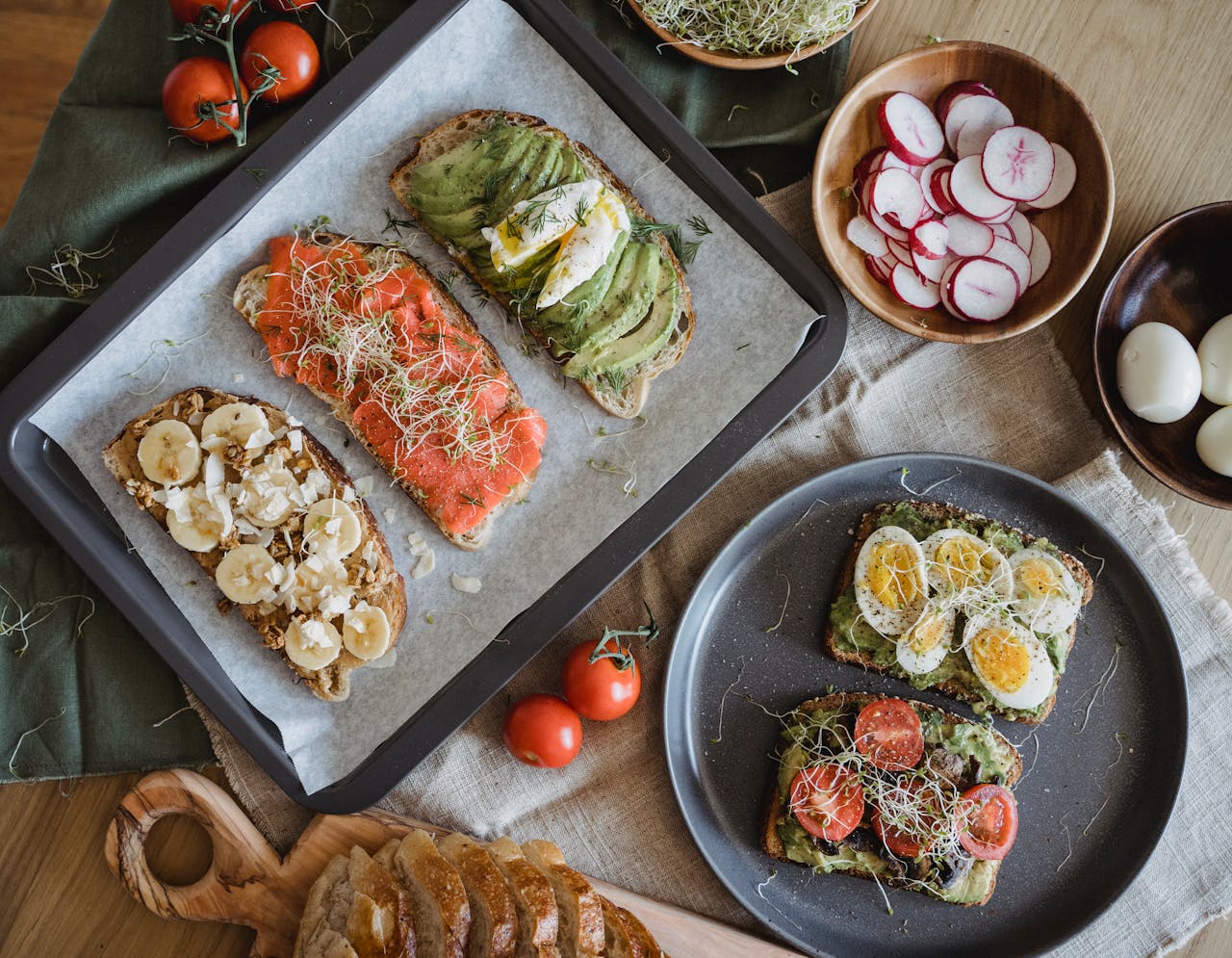 A variety of savory and sweet toasts with avocado, banana, eggs, and fresh toppings on a wooden table.